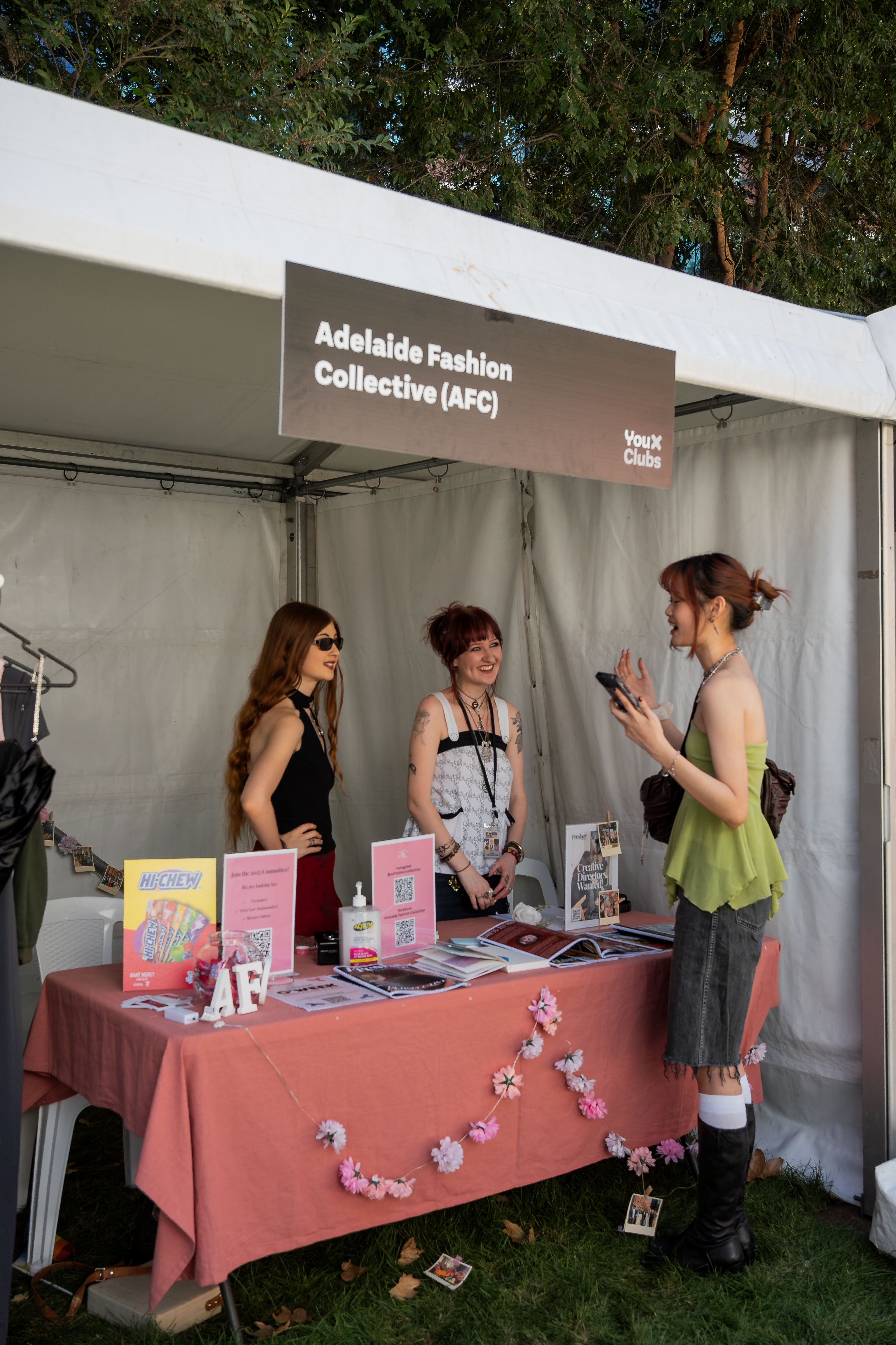 Four students stand side by side holding handmade masks and a punch card at a YouX Event on the Barr Smith Lawns