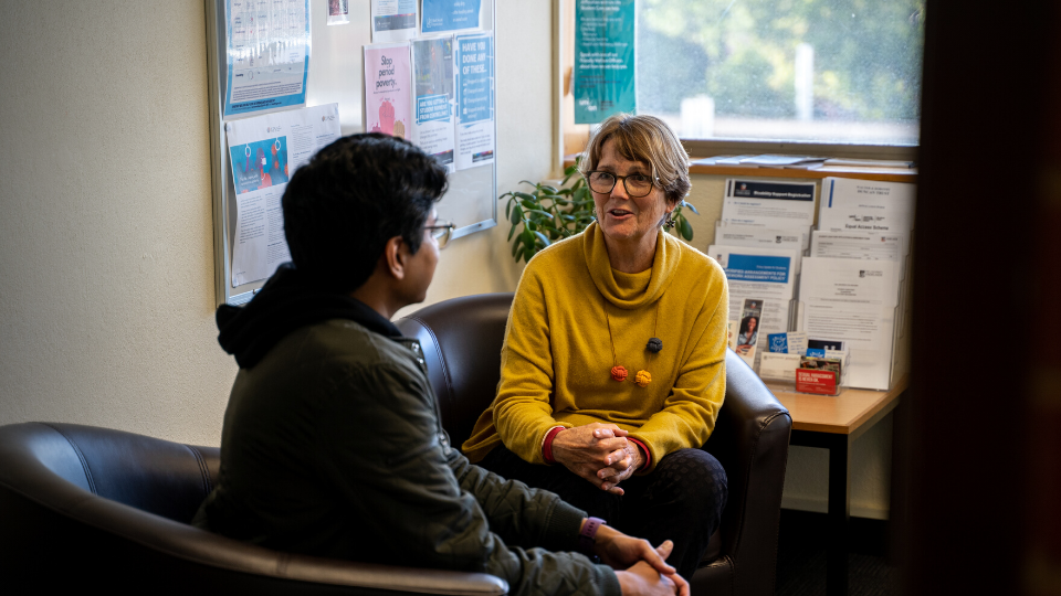 A Student Care staff member sits in front of a seated student in mid-conversation.